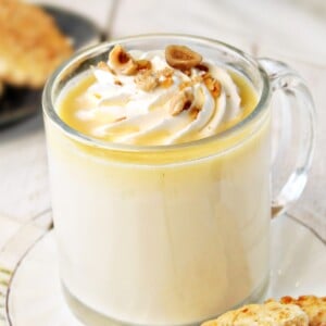 Mug of Hazelnut White Hot Chocolate with cookies in the background.