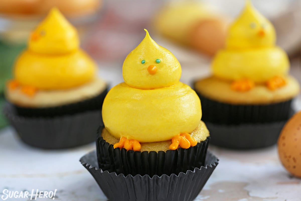 Three Baby Chick Cupcakes in black wrappers on a marble surface.