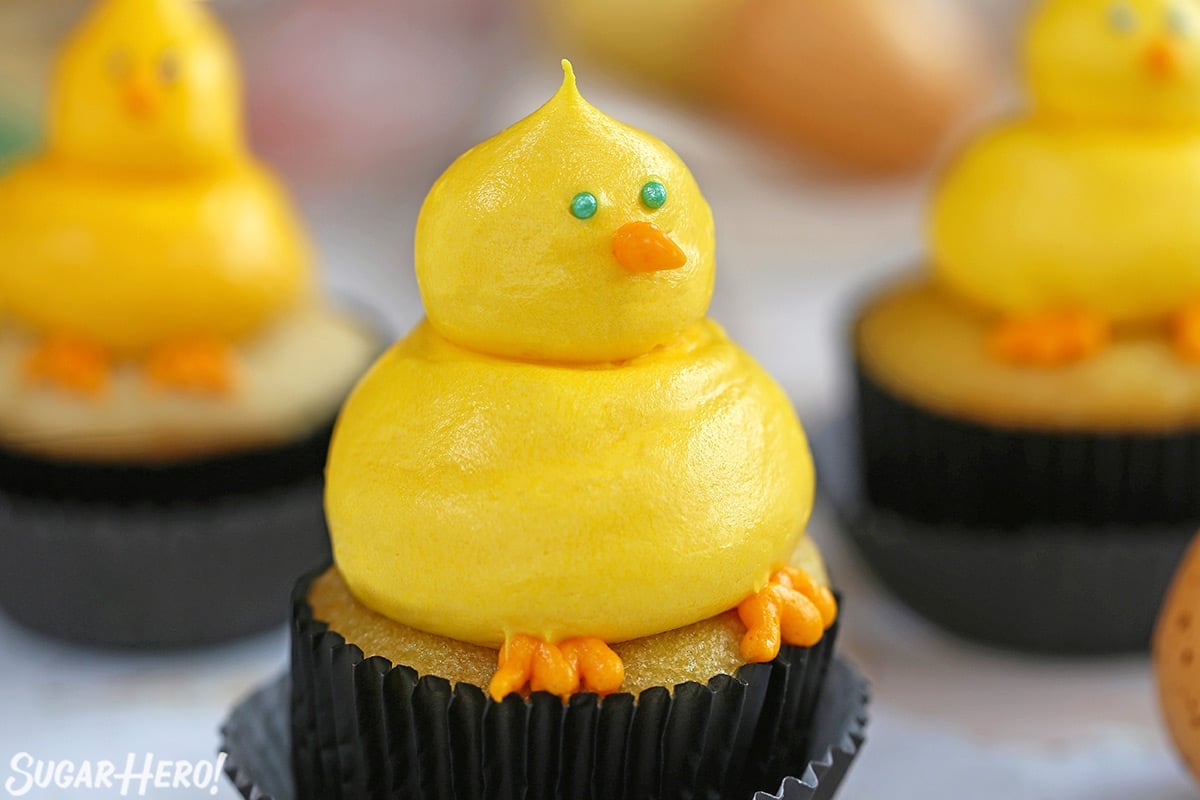 Three Baby Chick Cupcakes made of yellow buttercream, on yellow cupcakes in black wrappers.