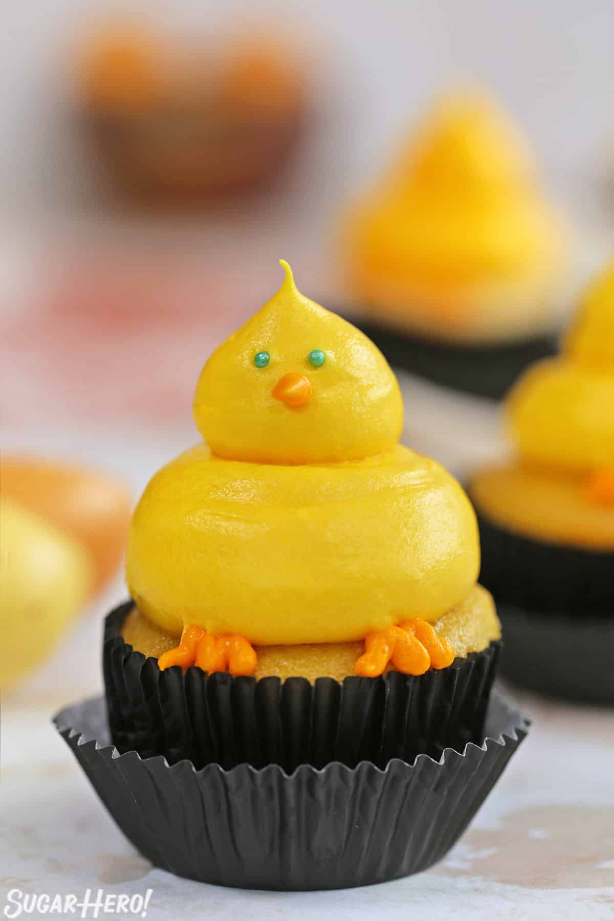 Close up of a Baby Chick Cupcake on a marble surface, with eggs in the background.