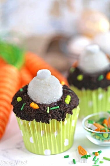 Bunny Butt Cupcakes next to a small bowl of Easter candy with decorative carrots in the background.