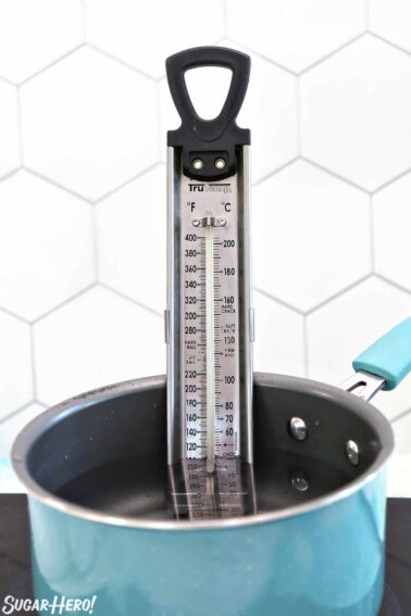 Tall candy thermometer in a a teal saucepan filled with water.