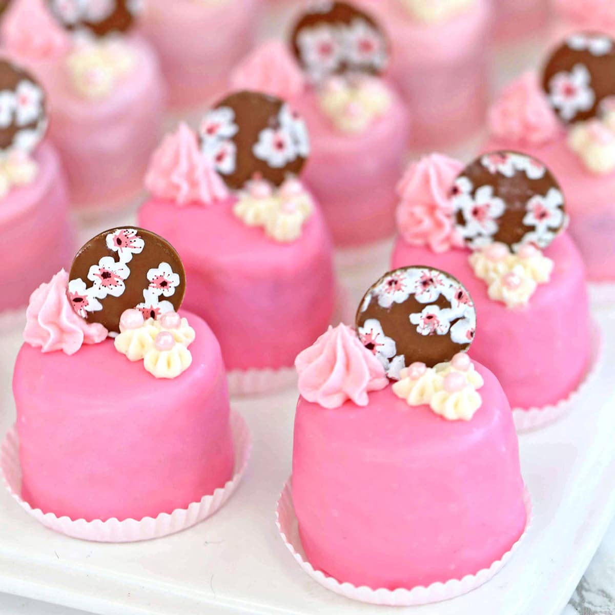 Cherry Blossom Petit Fours in small white candy cups on a white platter.