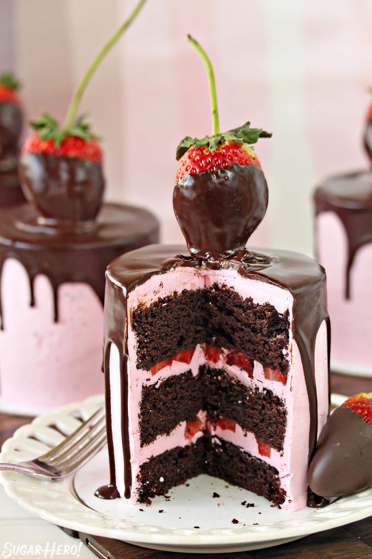 Chocolate-Covered Strawberry Cake on a white plate, cut open to show the cake and buttercream layers inside.
