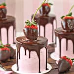 Close-up of mini cake with pink strawberry buttercream, a chocolate drip, and a large chocolate strawberry on top.