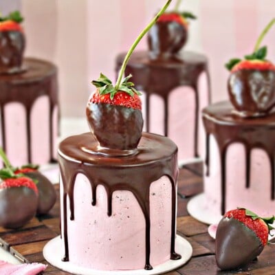 Close-up of mini cake with pink strawberry buttercream, a chocolate drip, and a large chocolate strawberry on top.
