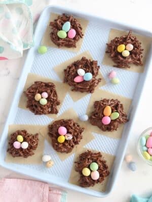 Overhead shot of Chocolate Easter Nests on brown parchment squares, arranged on a blue baking sheet.