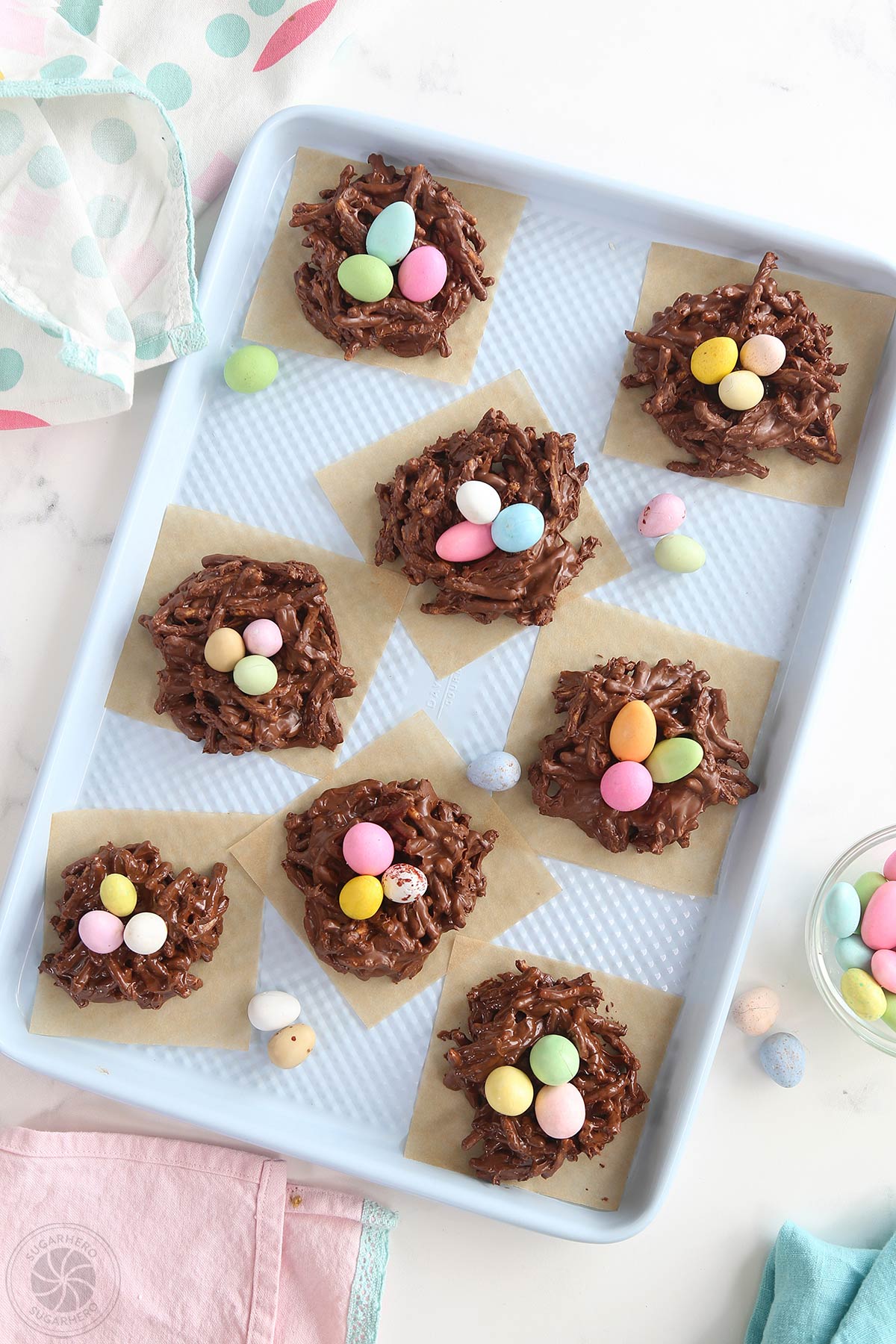 Overhead shot of Chocolate Easter Nests on brown parchment squares, arranged on a blue baking sheet.