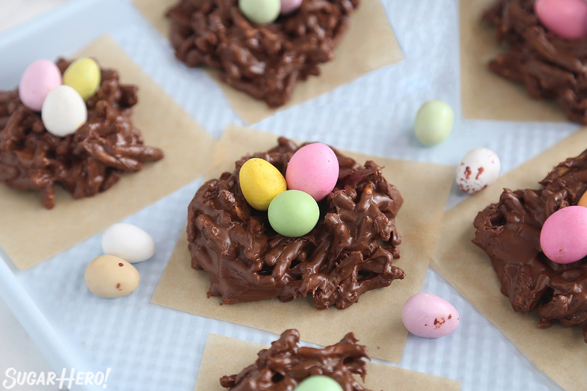 A group of Chocolate Nests on brown parchment squares with candy eggs scattered around.