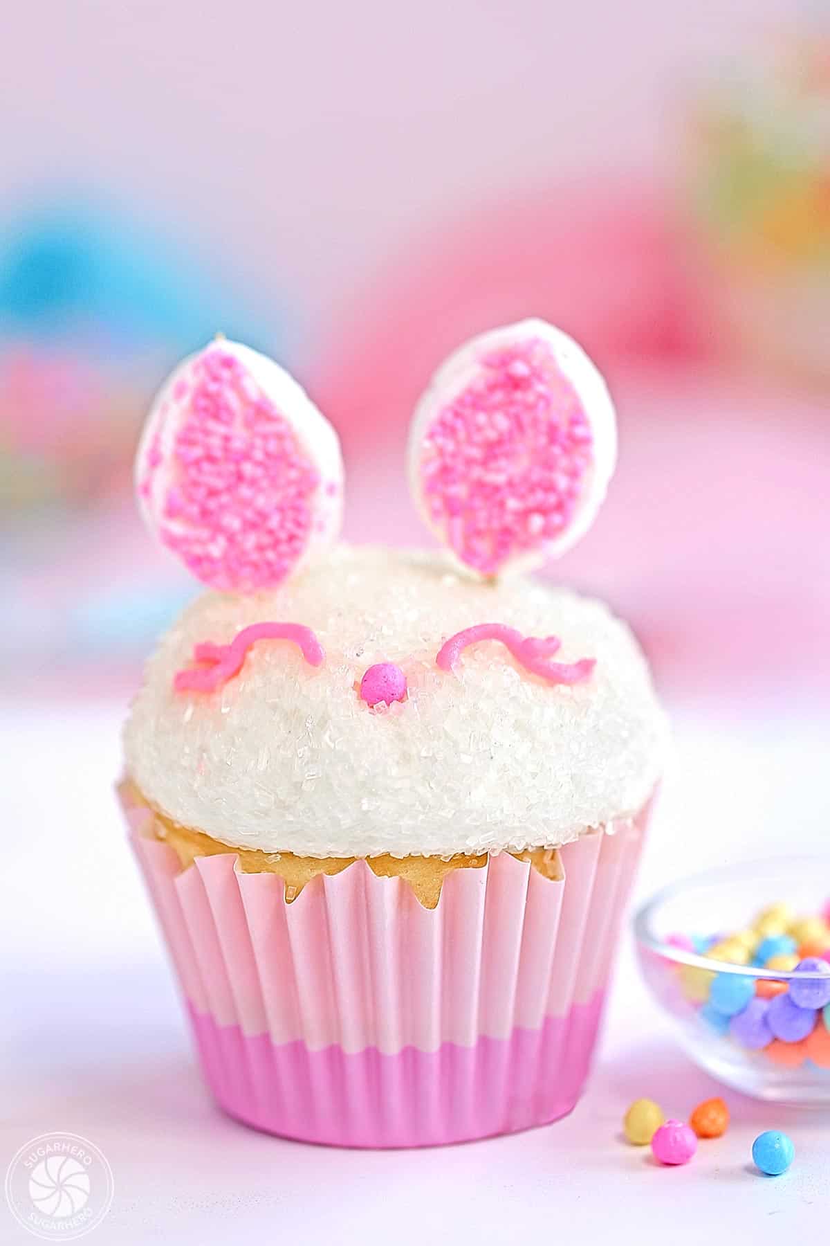 Close up of an Easter Bunny Cupcake next to a small bowl of sprinkles.