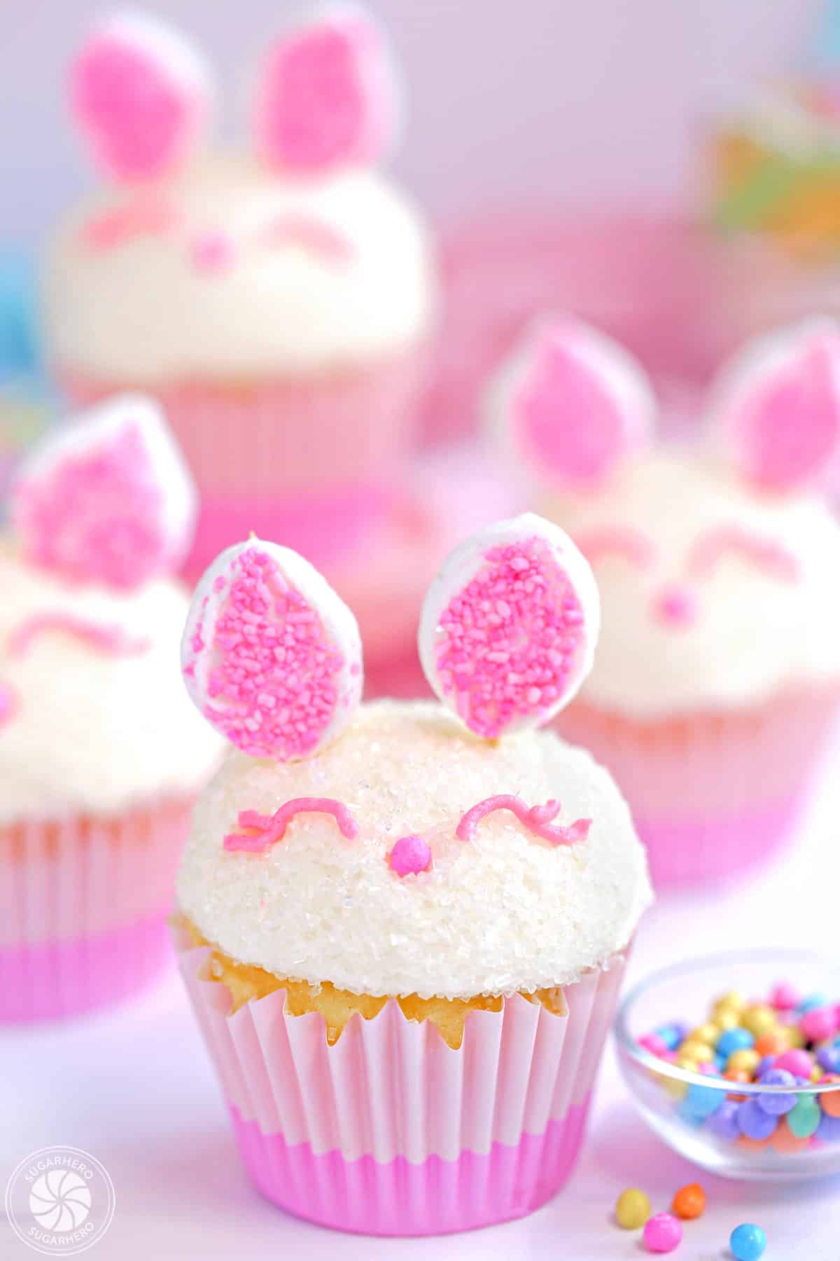 4 Easter Bunny Cupcakes next to a small bowl of sprinkles.