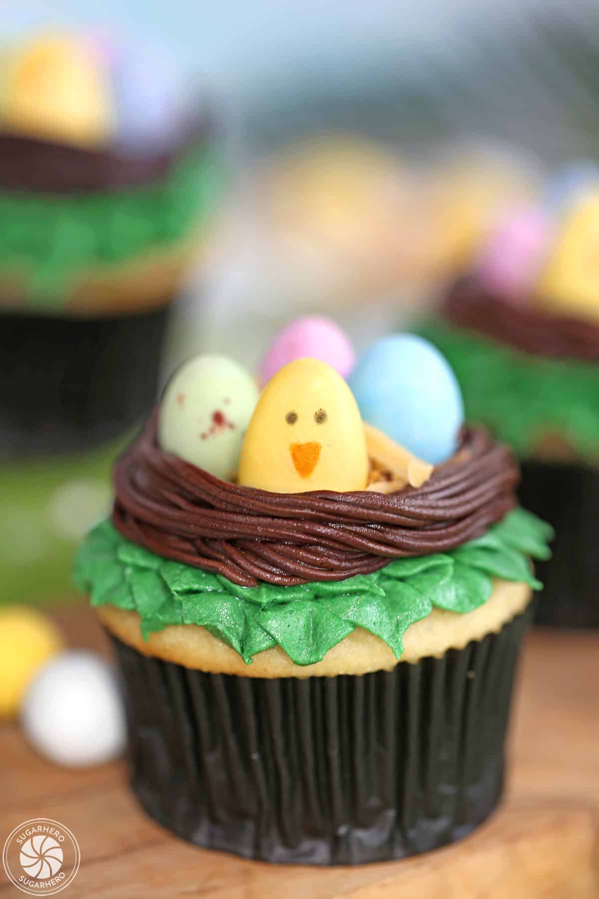 Easter Bird's Nest Cupcakes filled with candy eggs, on a wooden surface.