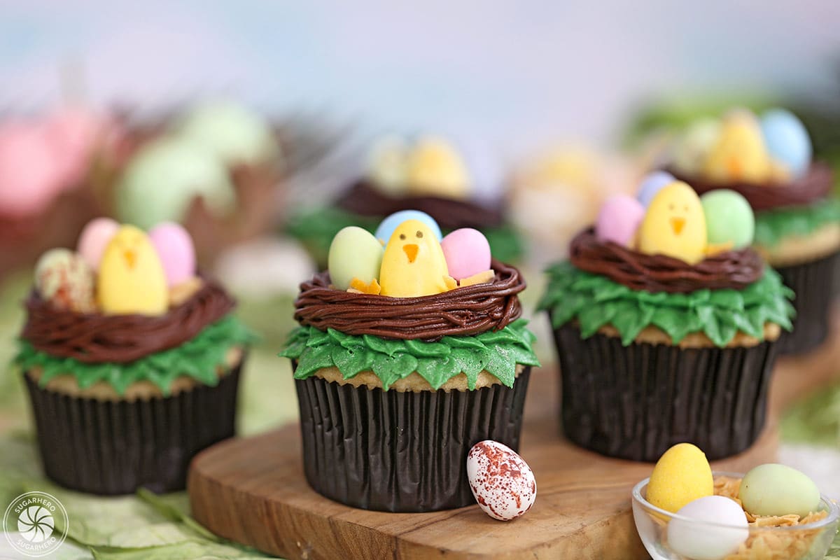 Easter Bird's Nest Cupcakes on a wooden surface with candy eggs and coconut around.