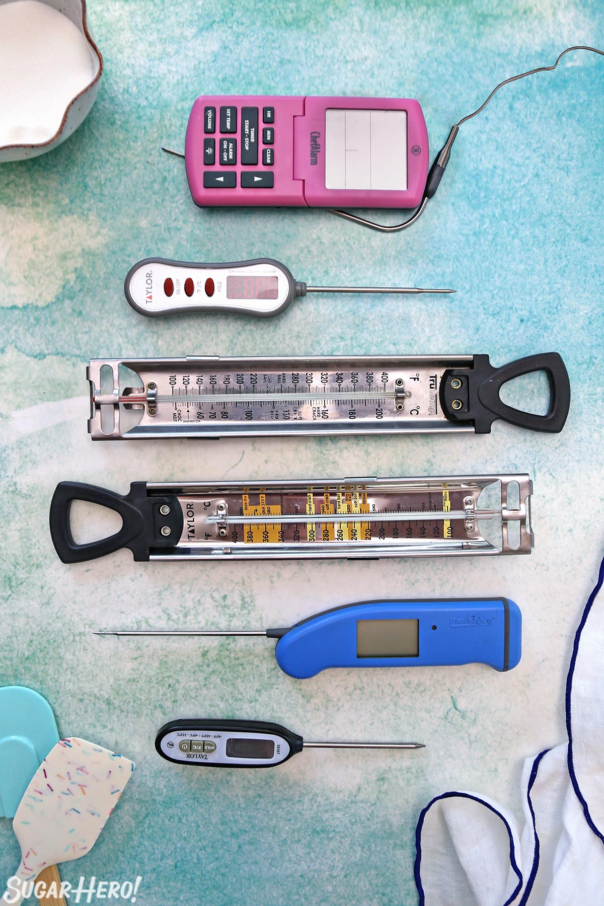 Overhead shot of six different candy thermometers on a blue-green background.