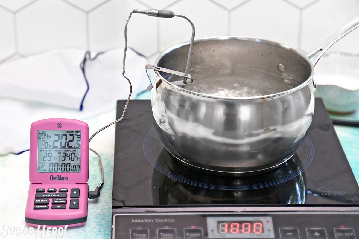 Pot of boiling candy with a thermometer probe inside and a pink thermometer to the left.