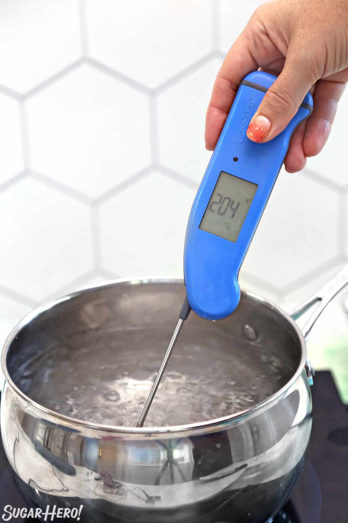 Pot of boiling candy with a hand holding a candy thermometer in the water.