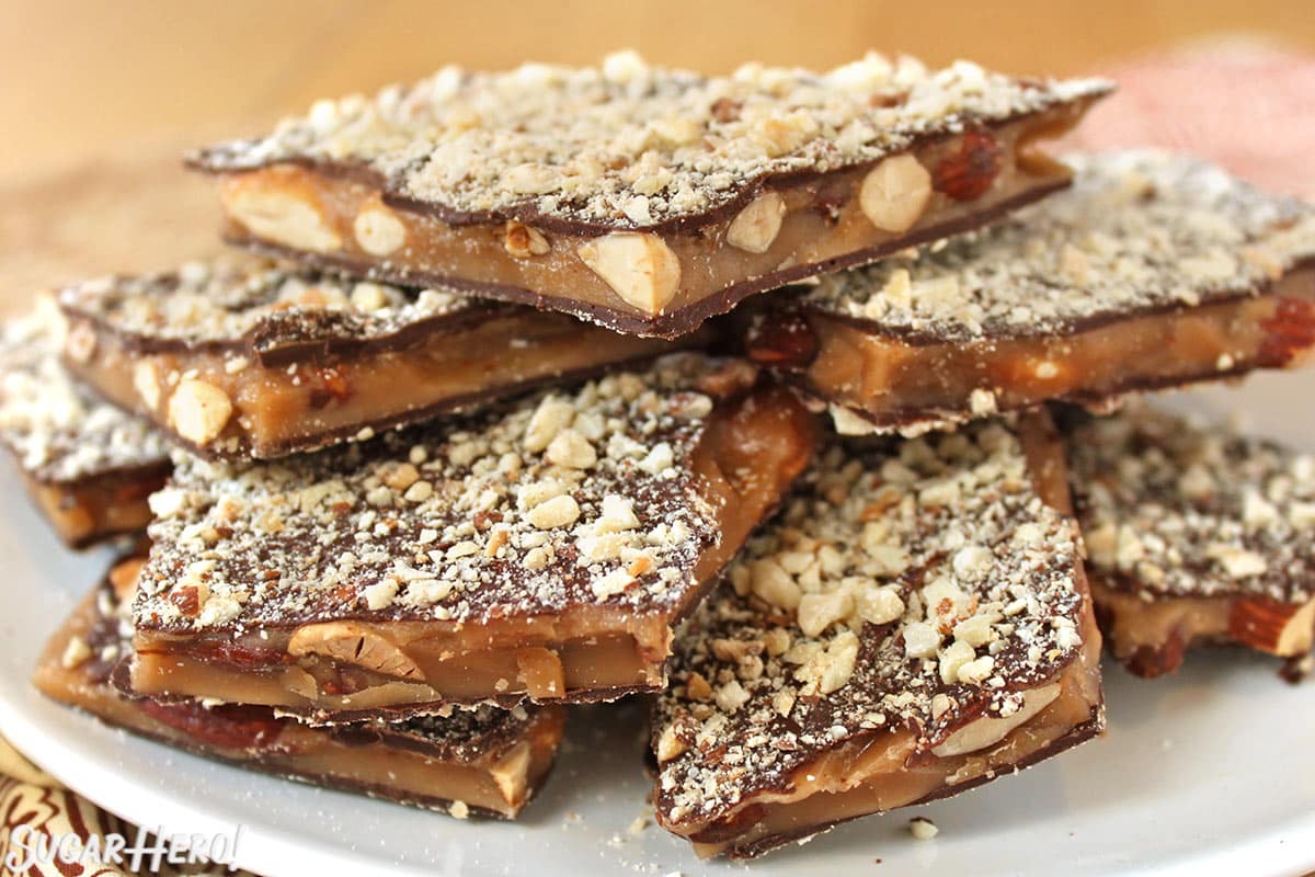 Close-up of almond toffee stacked on top of itself on a white plate.