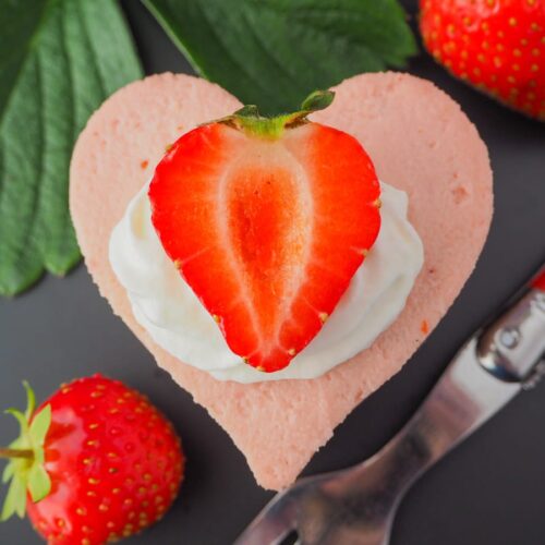 Close up of a heart-shaped Mini Strawberry Cheesecake next to a fork and strawberry.