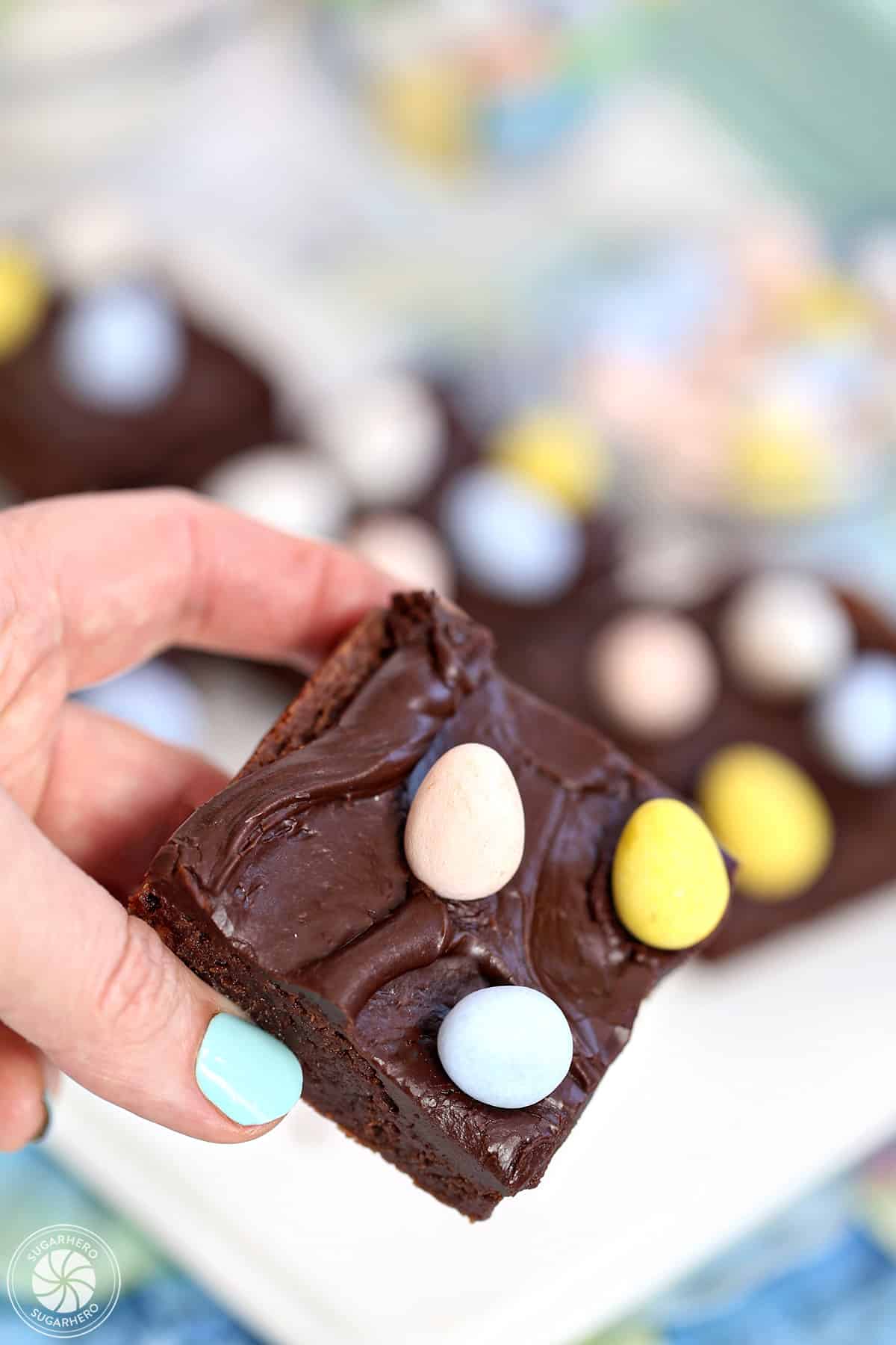 Hand holding up a brownie with chocolate frosting and chocolate eggs on top.