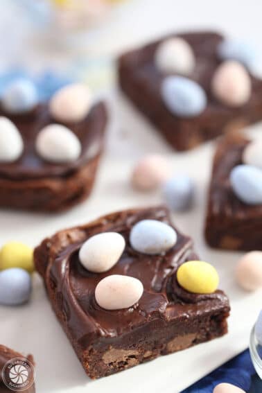 Four Easter Egg Brownies on a white platter with Cadbury mini eggs scattered on top and around them.