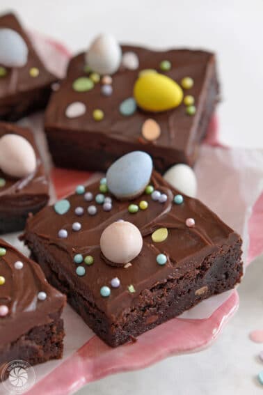 Four Easter Egg Brownies on a white platter with Cadbury mini eggs scattered on top and around them.