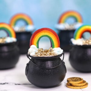 Group of Pot of Gold Cake Cups on a white marble surface with a blue cloud background.
