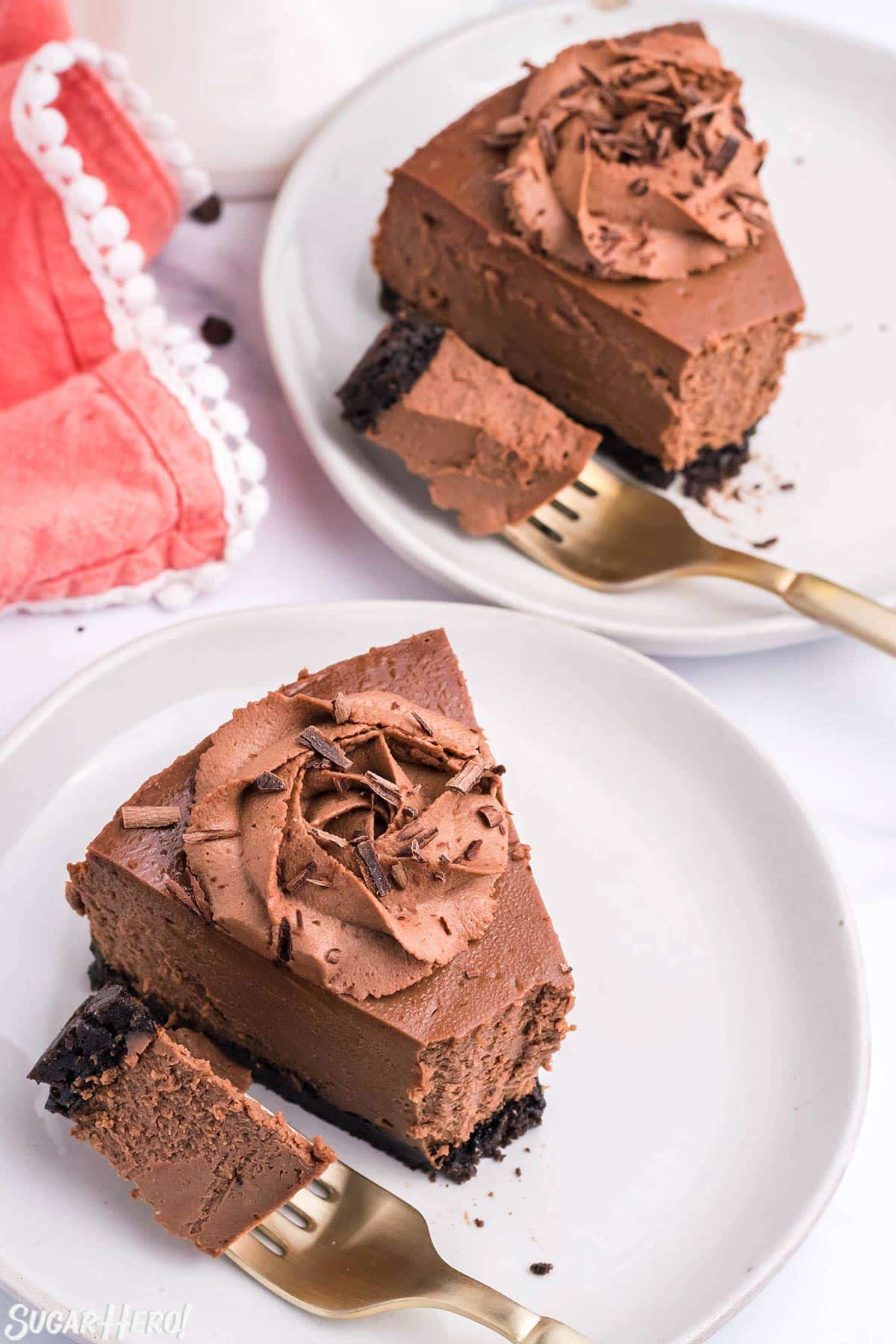 2 slices of Chocolate Cheesecake on white plates with forks holding bites of cheesecake to show texture.
