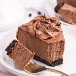 Close up of a slice of Chocolate Cheesecake on a white plate with a fork holding a bite on a fork.