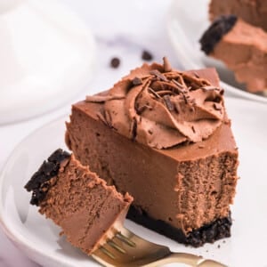 Close up of a slice of Chocolate Cheesecake on a white plate with a fork holding a bite on a fork.