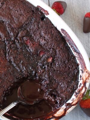 Top view of a Chocolate Strawberry Pudding Cake with a spoon inserted to show chocolate pudding sauce.