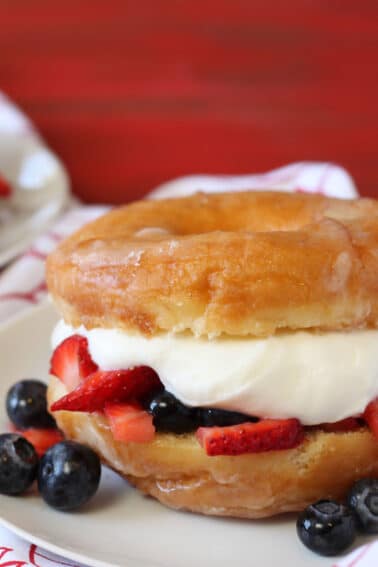 Close up of a Doughnut Strawberry Shortcake on white plate with a red backdrop.