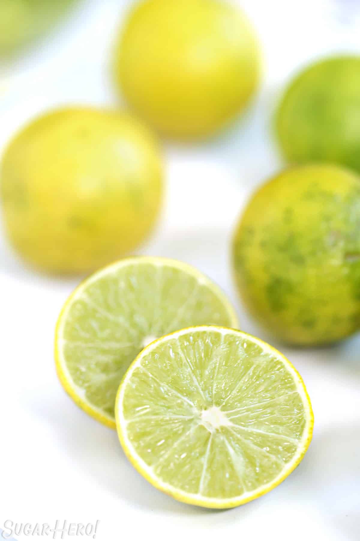 A key lime cut in half on a white background, with whole key limes behind the halves.