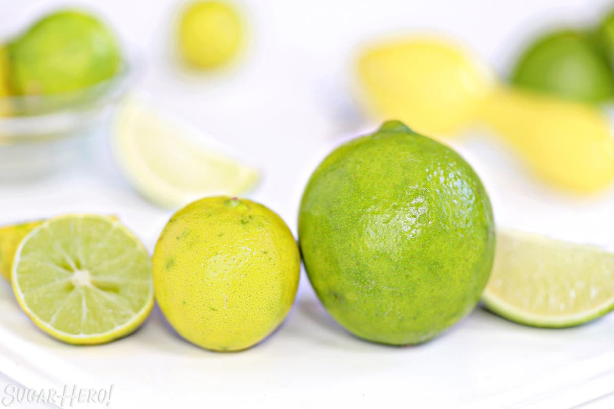 Two different limes next to each other: a small yellow key lime on the left, and a larger green Persian lime on the right.