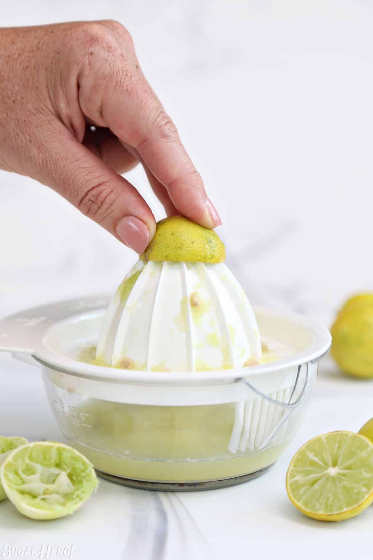 Hand juicing a key lime on a white marble background.