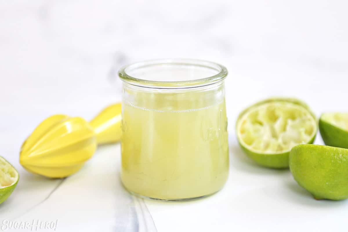 Key lime juice in a small glass jar, with lime halves and a citrus reamer in the background.