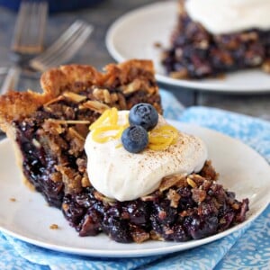 Close up of blueberry crumble pie topped with whipped cream, fresh blueberries and lemon zest.