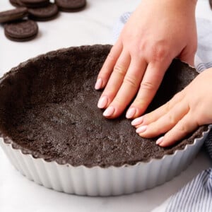 Two hands pressing Oreo crust into a fluted tart pan.