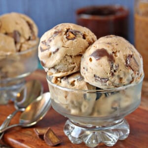 Several large scoops of Peanut Butter Cup Ice Cream in a glass dessert bowl next to silver spoons.