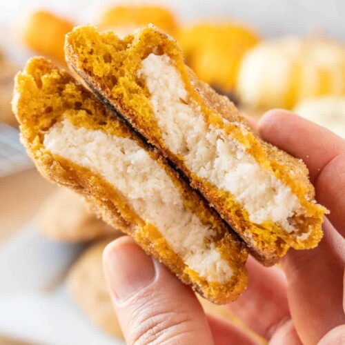Hand holding a pumpkin cheesecake cookie, split in two to show the inside.
