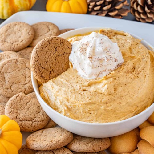 White bowl of Pumpkin Fluff Dip with cookies scattered on a platter around it.