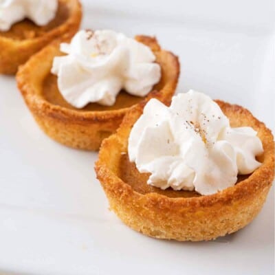 Three Pumpkin Pie Cookie Cups topped with whipped cream, on a white surface.