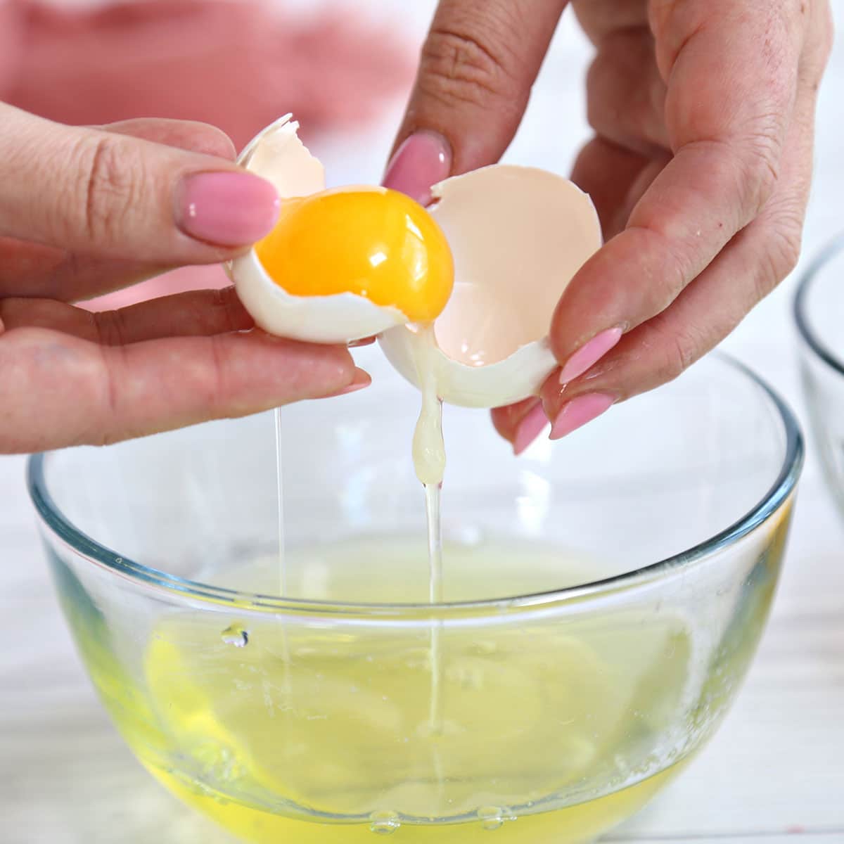 Hands using an eggshell to separate egg yolks from egg whites.