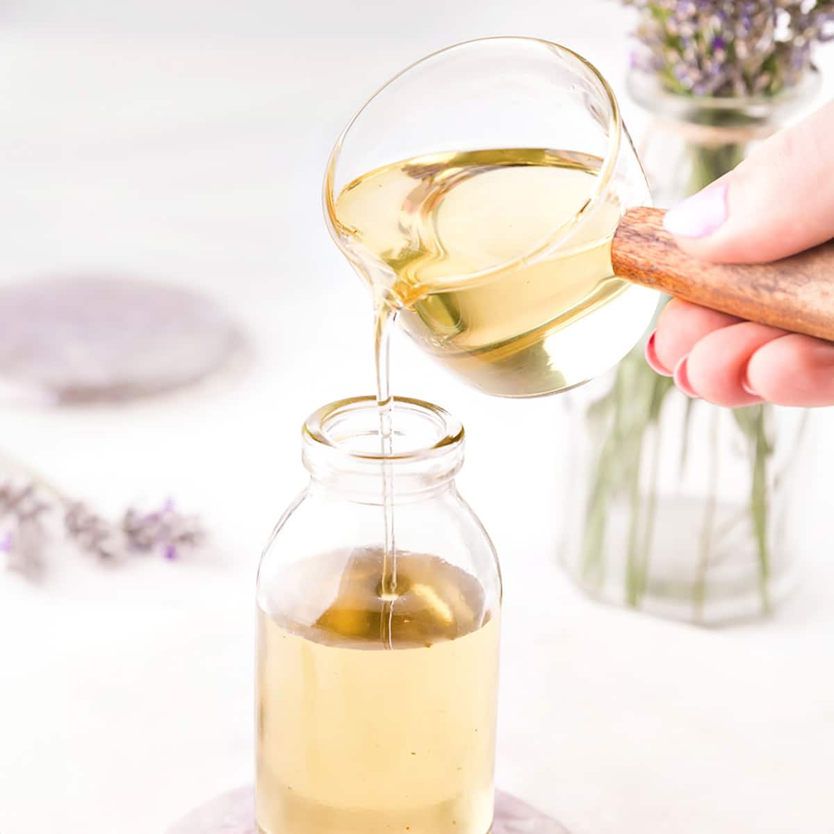 Pouring lavender simple syrup from a measuring cup into a glass jar.