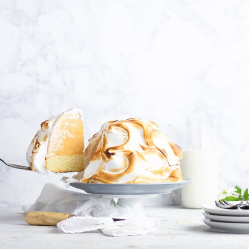 Pumpkin Baked Alaska on a white cake stand, with one slice being removed on a cake server.