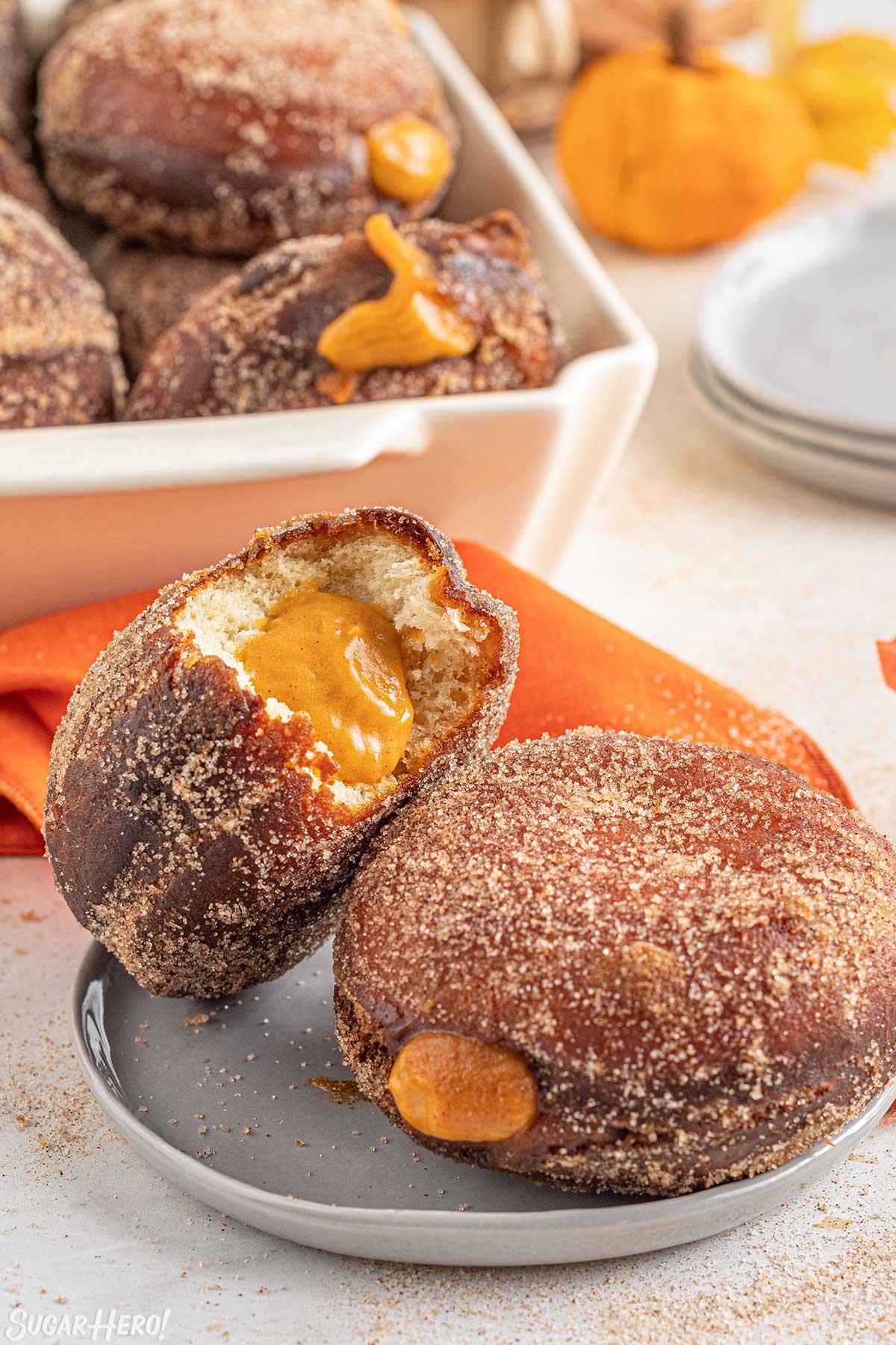 2 Pumpkin Cream Filled Donuts on a small gray plate with one leaning against the other and a bite removed from one to show the pumpkin filling.