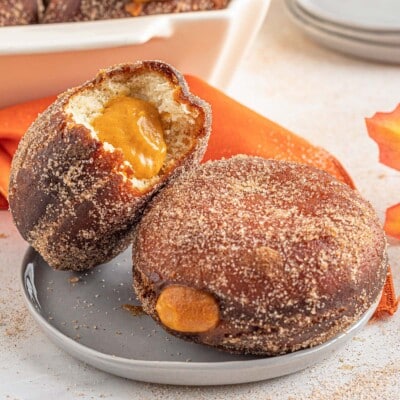 2 Pumpkin Cream Filled Donuts on a small gray plate with one leaning against the other and a bite removed from one to show the pumpkin filling.