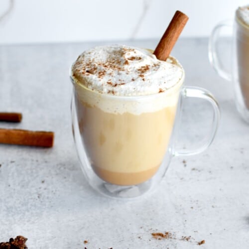 Coffee drink with pumpkin spice whipped cream and a cinnamon stick on top.