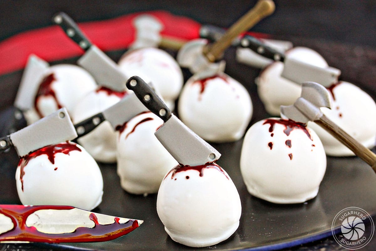 Bloody Halloween Cake Ball Truffles on a black plate, with candy weapons sticking out of them.