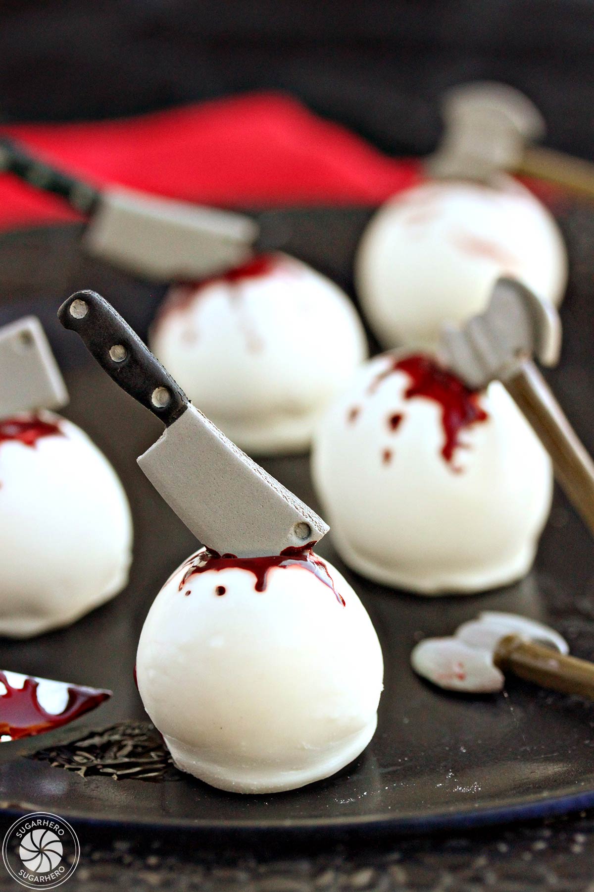 Five Bloody Halloween Cake Ball Truffles on a black plate with a red linen in the background.