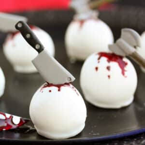 Halloween Cake Ball Truffles on a black plate, decorated with candy weapons and food coloring blood.